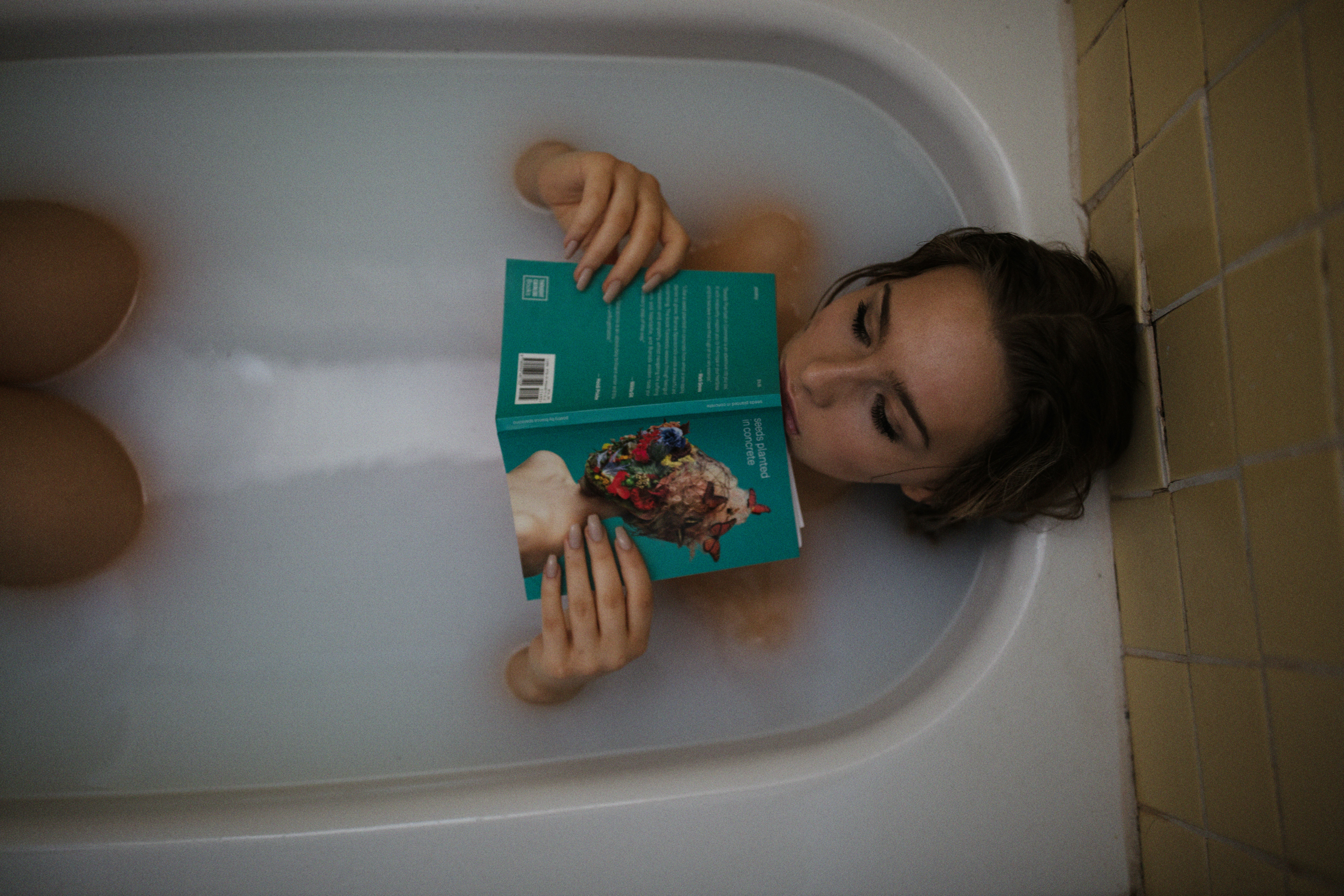 woman lying on bathtub with green book